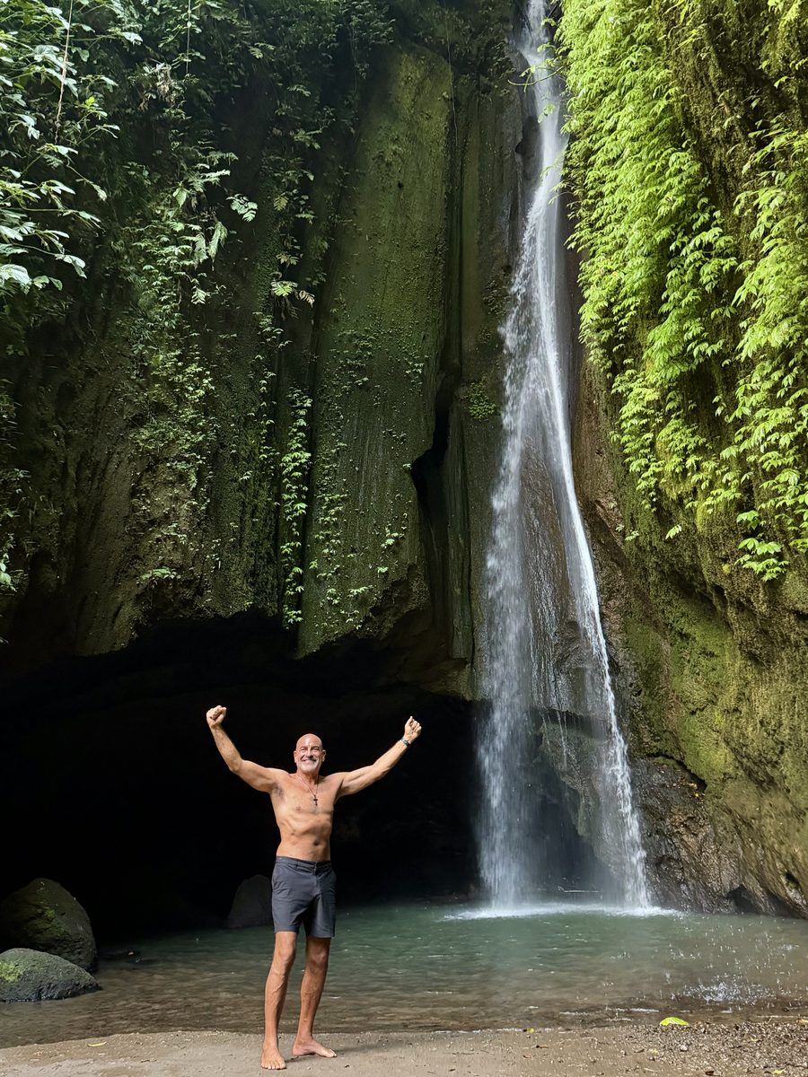 Brian Fabiano, arms raised, barefoot beneath a waterfall